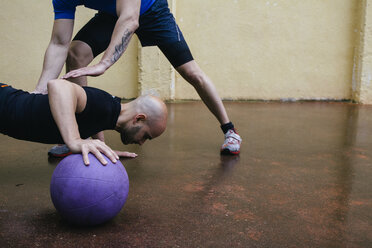 Mann macht Liegestütze mit einem Medizinball, unterstützt von einem Trainer - ABZF000379