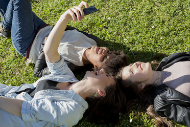 Drei Freundinnen liegen im Gras und machen ein Selfie mit ihrem Smartphone - MAUF000445