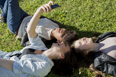 Three girl friends lying on grass taking selfie with smart phone - MAUF000445