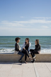 Drei junge Frauen, die am Meer sitzen und sich unterhalten - MAUF000448