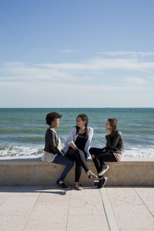 Drei junge Frauen, die am Meer sitzen und sich unterhalten - MAUF000448