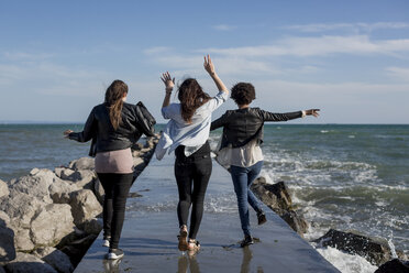 Drei junge Frauen vergnügen sich auf einem Wellenbrecher am Meer - MAUF000455
