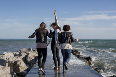 Drei junge Frauen vergnügen sich auf einem Wellenbrecher am Meer - MAUF000456