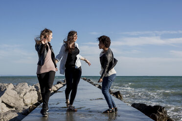 Drei junge Frauen vergnügen sich auf einem Wellenbrecher am Meer - MAUF000457