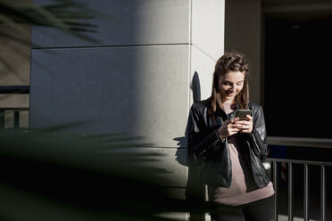 Junge Frau lehnt an der Wand und benutzt ein Smartphone - MAUF000479