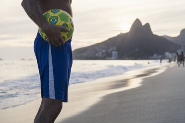 Brazil, Rio De Janeiro, man holding ball on Ipanema beach - MAUF000496