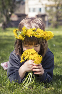 Little girl with floral wreath lying on meadow smelling dandelions - LVF004779