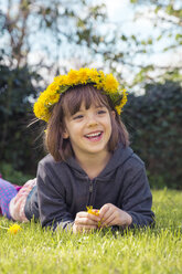 Portrait of smiling little girl lying on meadow wearing floral wreath of dandelions - LVF004781