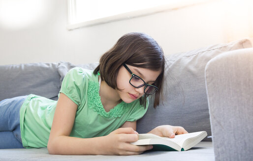 Girl lying on the couch reading a book - LVF004789