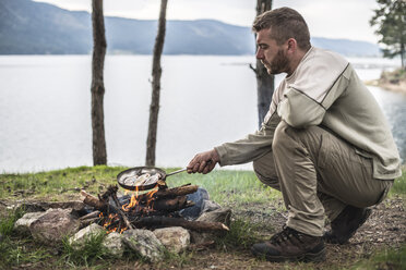 Bulgaria, man frying rudd at camp fire at shore of Dospat Reservoir - DEGF000785