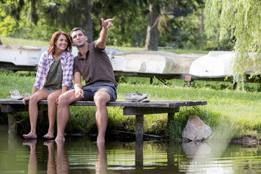 Junges Paar sitzt auf einem Steg am See und schaut in die Ferne - ZOCF000049