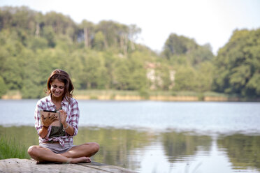Junge Frau mit digitalem Tablet sitzt auf einem Steg am See - ZOCF000056