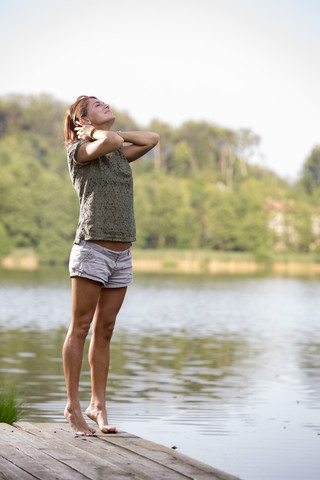 Junge Frau streckt sich auf einem Steg am See am Morgen, lizenzfreies Stockfoto