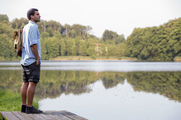 Junger Mann steht auf einem Steg am See und schaut in die Ferne - ZOCF000059