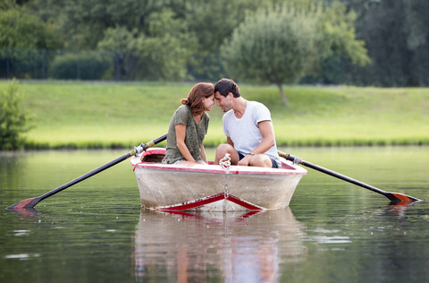 Junges Paar von Angesicht zu Angesicht in einem Ruderboot auf dem See, lizenzfreies Stockfoto