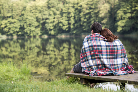 Rückenansicht eines jungen Paares, das auf einem Steg am See sitzt, lizenzfreies Stockfoto