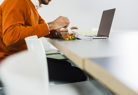 Junger Mann isst einen Salat am Schreibtisch im Büro, lizenzfreies Stockfoto