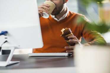 Junger Mann mit einem Snack am Schreibtisch im Büro - UUF007104