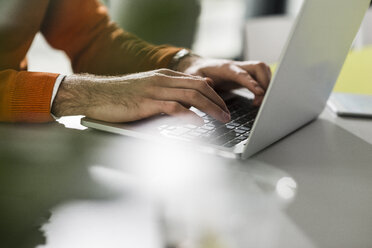 Junger Mann mit Laptop am Schreibtisch im Büro - UUF007107