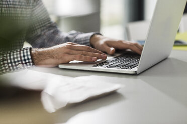 Junger Mann mit Laptop am Schreibtisch im Büro - UUF007108