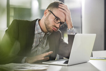 Unzufriedener junger Mann mit Laptop im Büro - UUF007109