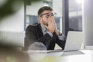 Erschöpfter junger Mann mit Laptop im Büro - UUF007110