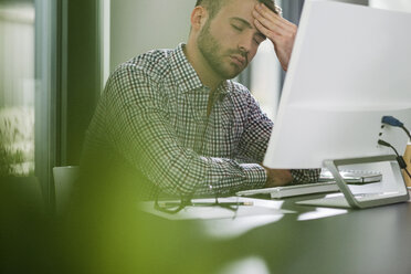 Müder junger Mann am Schreibtisch im Büro - UUF007112