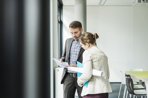 Zwei Kollegen diskutieren im Büro über ein Papier, lizenzfreies Stockfoto