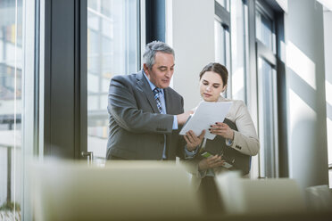 Senior businessman and young businesswoman discussing papers - UUF007135