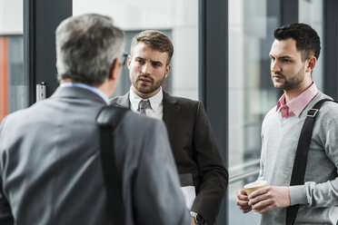 Three businessmen talking on office floor - UUF007148