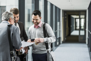 Three businessmen talking on office floor - UUF007149