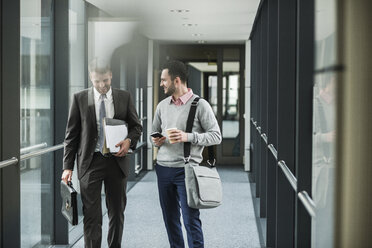 Zwei Kollegen, die auf der Büroetage gehen und sich unterhalten - UUF007151