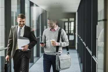 Zwei Kollegen, die auf der Büroetage gehen und sich unterhalten - UUF007152