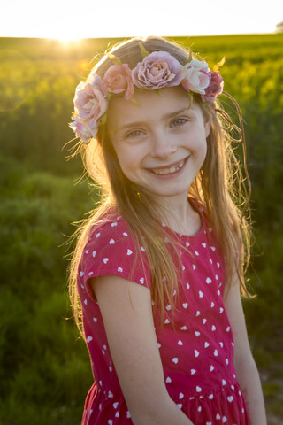 Porträt eines lächelnden Mädchens mit Blumenkranz in einem Rapsfeld, lizenzfreies Stockfoto