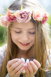 Portrait of smiling girl with wreath of flowers holding magnolia blossom in her hands - SARF002700