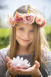 Portrait of smiling girl with wreath of flowers holding magnolia blossom in her hands - SARF002701