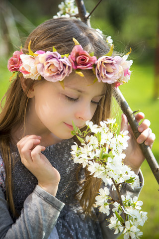 Kleines Mädchen mit Blumenkranz riecht an einem blühenden Zweig, lizenzfreies Stockfoto