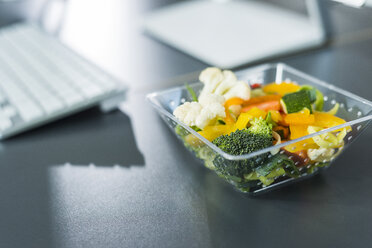 Plastic bowl with vegetables on desk in office - UUF007222