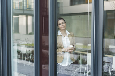 Weiblicher leitender Angestellter an einer Fensterscheibe stehend, Kaffeetasse - UUF007228