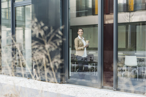 Female senior manager standing on window pane, coffee cup - UUF007229