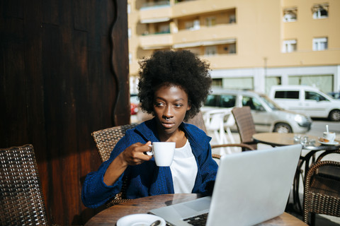 Junge Frau mit Laptop sitzt in einem Straßencafé und trinkt Kaffee, lizenzfreies Stockfoto