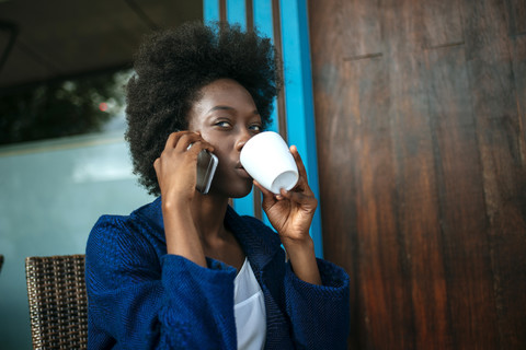 Porträt einer jungen Frau, die in einem Straßencafé mit ihrem Handy telefoniert und Kaffee trinkt, lizenzfreies Stockfoto