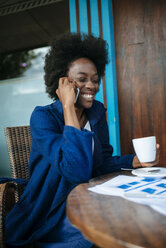 Porträt einer jungen Frau, die in einem Straßencafé mit ihrem Handy telefoniert und Kaffee trinkt - KIJF000340