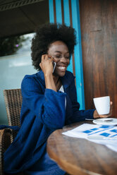 Portrait of young woman talking on mobile phone while drinking coffee in a street cafe - KIJF000340