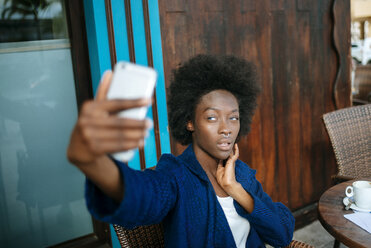 Porträt einer jungen Frau, die ein Selfie mit ihrem Smartphone in einem Straßencafé macht - KIJF000342