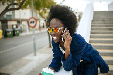 Porträt einer jungen Frau mit verspiegelter Sonnenbrille, die mit einem Mobiltelefon spricht - KIJF000345