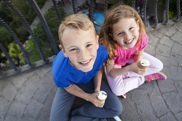 Porträt von Bruder und Schwester mit Eistüten auf dem Balkon sitzend und zur Kamera aufblickend - VABF000472