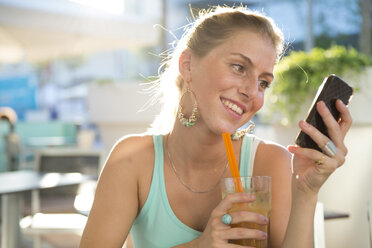 Blond young woman at outdoor cafe looking at her smartphone - ZOCF000075