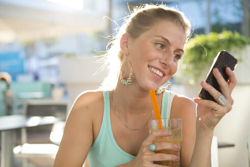 Blonde junge Frau in einem Straßencafé, die auf ihr Smartphone schaut - ZOCF000075