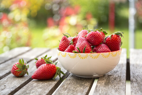 Bowl of strawberries on wooden garden table - SARF002704